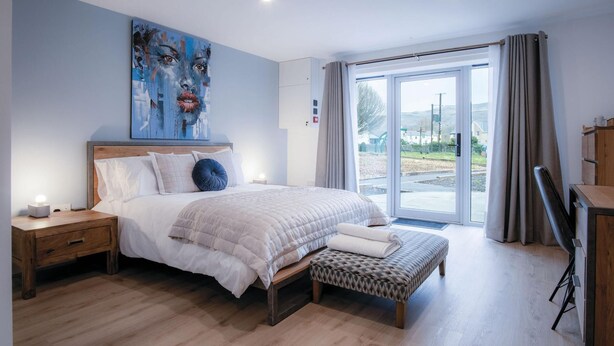Un dormitorio moderno con una cama grande, un banco, una mesita de noche y un cuadro en la pared.