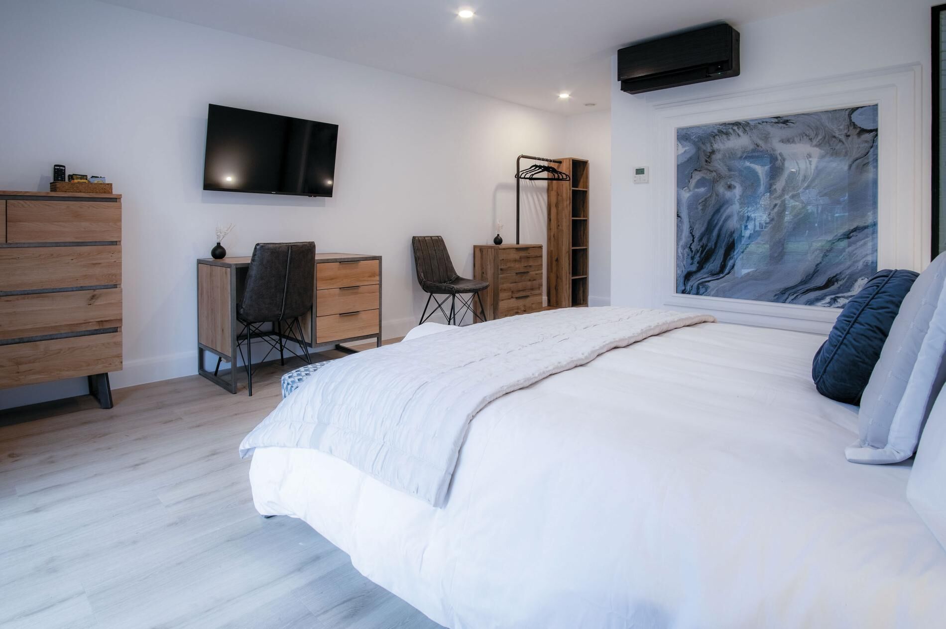 A bedroom with a large bed, a desk, a chair, a wardrobe, a TV, and a painting.
