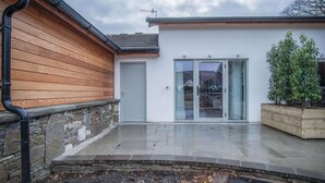 Un edificio moderno con fachada de madera, cimientos de piedra y un patio empedrado.