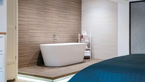 Un baño moderno con una bañera independiente, paneles de madera y un estante blanco con toallas.