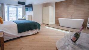 Un dormitorio moderno con una cama grande, televisión integrada, armario y baño con bañera independiente.