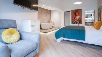 Ein modernes Schlafzimmer mit Bett, Sofa, Fernseher und Bad.