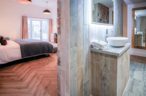 A modern bedroom with a large bed, a desk, and a bathroom with a large sink and mirror.