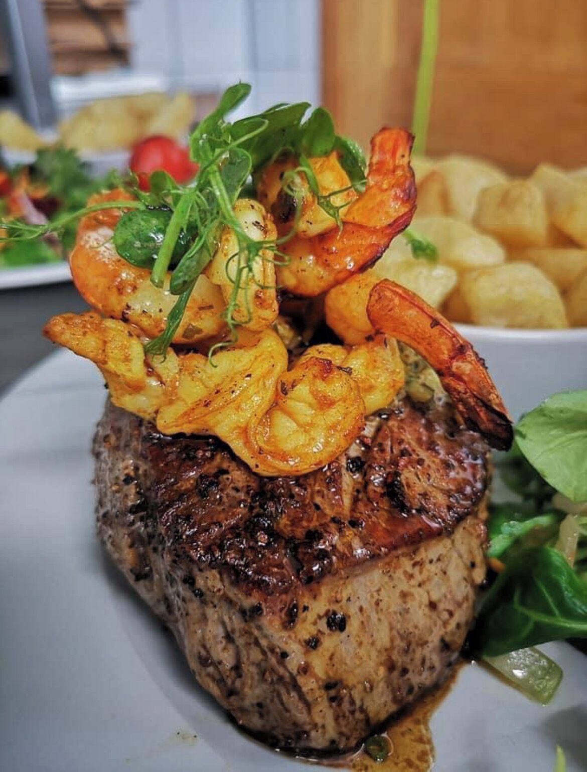 Bistec cubierto de camarones a la parrilla y verduras, acompañado de papas fritas.