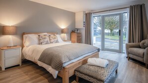 Ein modernes Schlafzimmer mit einem großen Bett, Nachttischlampen, einer Holzbank und Blick durch eine Glastür.
