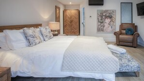 Une chambre spacieuse avec un grand lit, une armoire en bois, une chaise et des œuvres d’art accrochées aux murs.