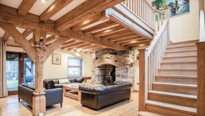 A spacious living area with a stone fireplace, wooden beams, and a staircase. - Oak Lodge - Hot Tub - Pen Y Cae Inn (Swansea Valley)