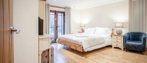 A bedroom with a wooden bed, bedside tables with lamps, a chair, and a large window with curtains.