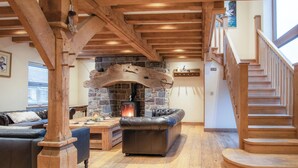 A cozy living room with a stone fireplace, leather sofa, wooden beams, and a staircase. - Oak Lodge - Hot Tub - Pen Y Cae Inn (Swansea Valley)