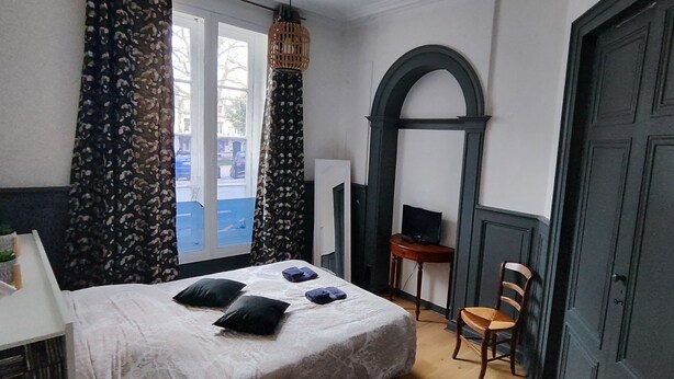 A bedroom with a bed, a chair, a desk, a television, and a door.