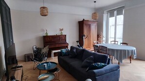 A living room with a dark blue sofa, a small round table, a wooden cabinet, and a dining table with chairs.