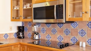A kitchen with a stainless steel microwave, wooden cabinets, a coffee maker, and a blender.