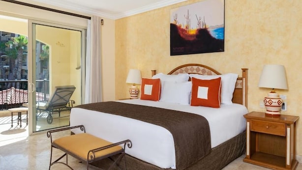 A hotel room with a bed, two bedside tables, a chair, a large window, and a balcony with a chair.