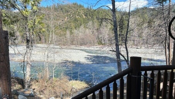 Une terrasse en bois surplombant une rivière, avec des arbres et une rive rocheuse.