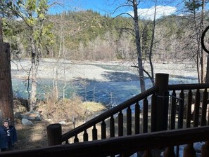 A wooden deck overlooking a river with trees and a rocky shoreline. - Cozy Log Cabin with private access to the Trinity River! (Trinity Center)