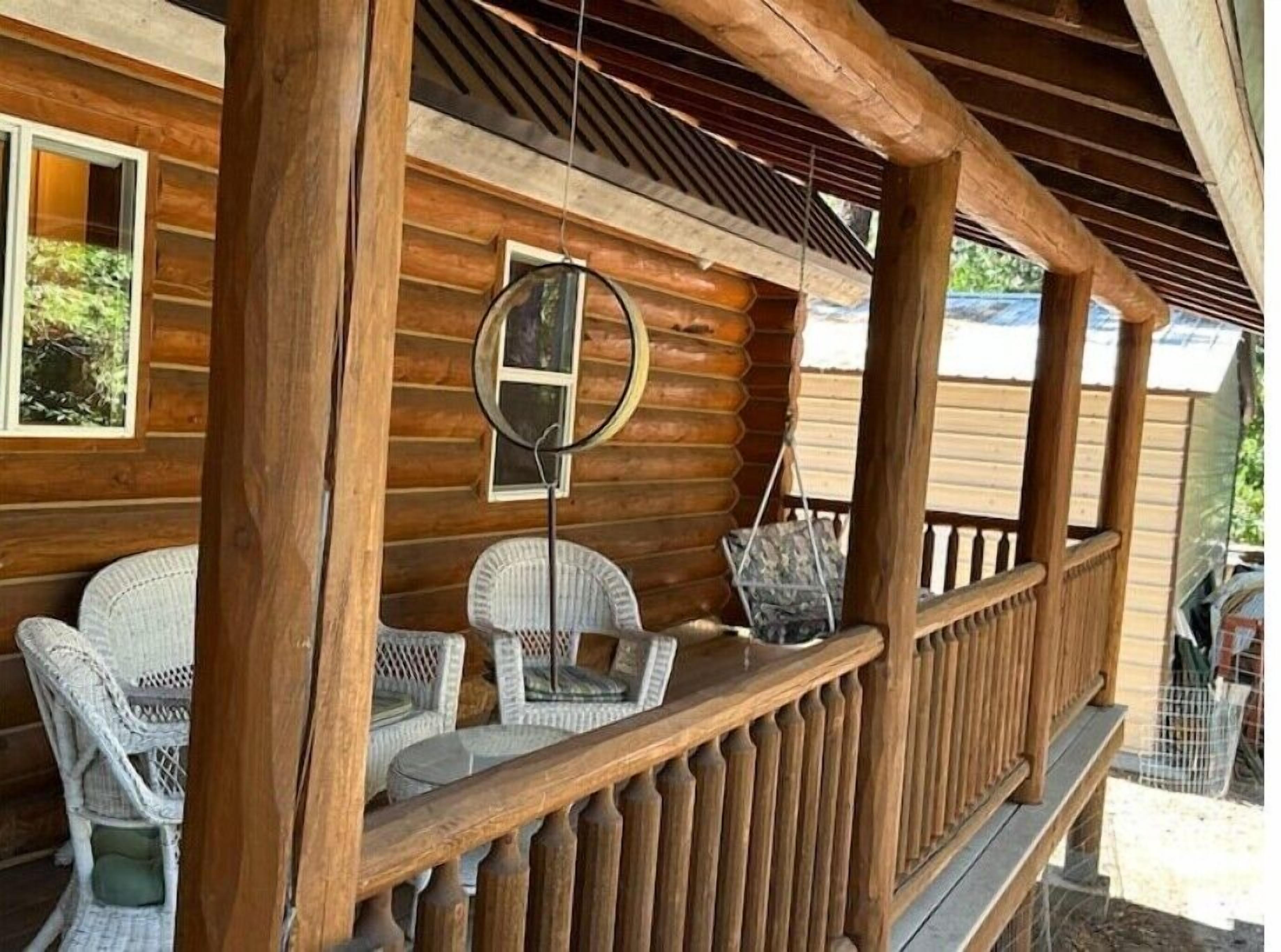 A wooden cabin with a porch featuring wicker chairs and a hanging mirror.