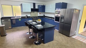Eine moderne Küche mit blauen Schränken, einer zentralen Kochinsel mit Barhocker, einem Edelstahlkühlschrank und einem eingebauten Ofen.