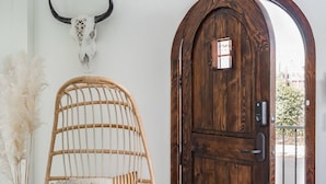 Un interior rústico con una puerta de madera, una silla tejida y un cráneo decorativo en la pared.