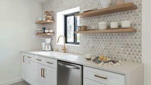 Una cocina moderna con armarios blancos, lavavajillas de acero inoxidable, estantes de madera con utensilios de cocina y un salpicadero geométrico.
