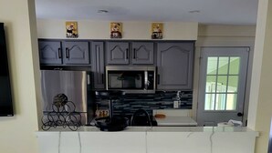 A modern kitchen with grey cabinets, a white marble countertop, and three black stools. - 14 Min to Lake Michigan: 3BR, 5 Beds, 30 Acres, Hot Tub, Sauna, Pets & Fire Pit (Covert)