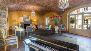 Ein großzügiges Wohnzimmer mit Klavier, bequemen Sitzgelegenheiten, einem Kamin und einem großen Fenster.