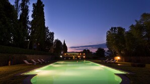 Ein Schwimmbecken im Abenddämmerung mit Liegestühlen und einem Gebäude im Hintergrund.