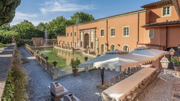 Ein Innenhof mit Pool, Sitzgelegenheiten im Freien und einem Gebäude mit Rundbogenfenstern.