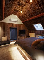 Un dormitorio con techo inclinado, una cama grande, un televisor y un tragaluz.