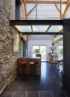 Un interior moderno con pared de piedra, taburetes de madera y zona de comedor con vistas al exterior.