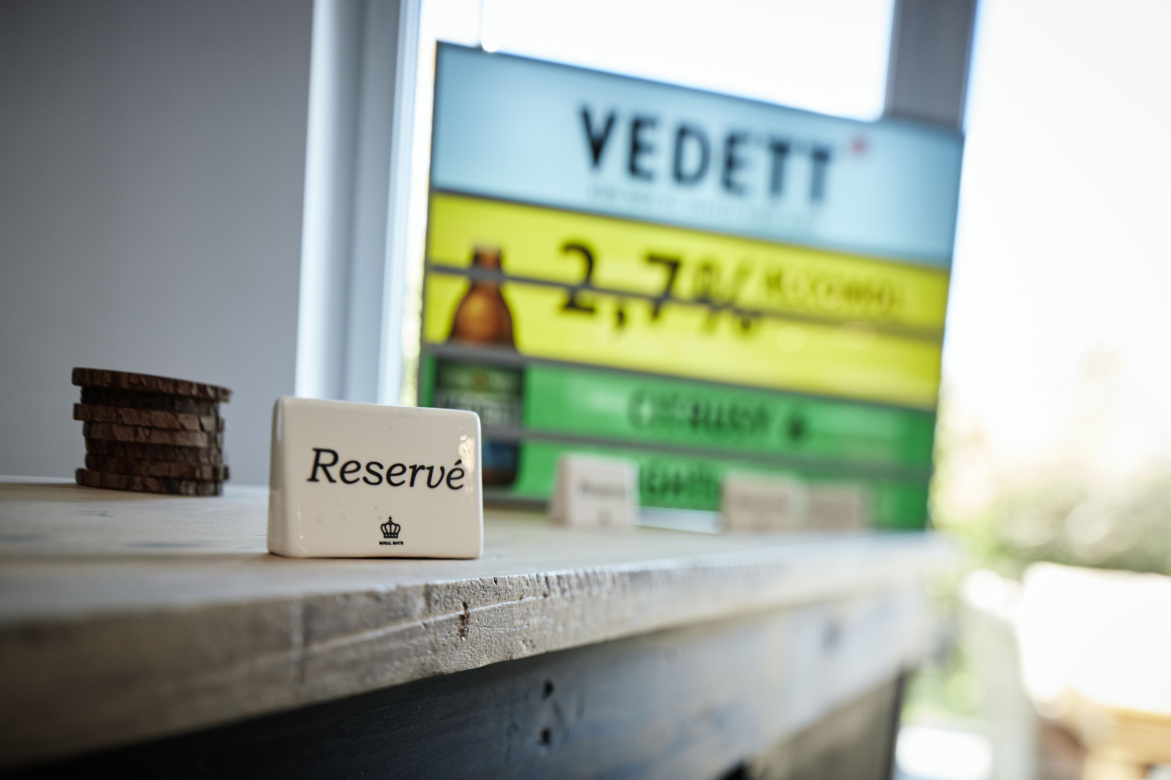 Uma pequena placa com a palavra 'Reserved' numa superfície de madeira, com um fundo desfocado mostrando uma placa com a palavra 'VEDETT' e algum texto.