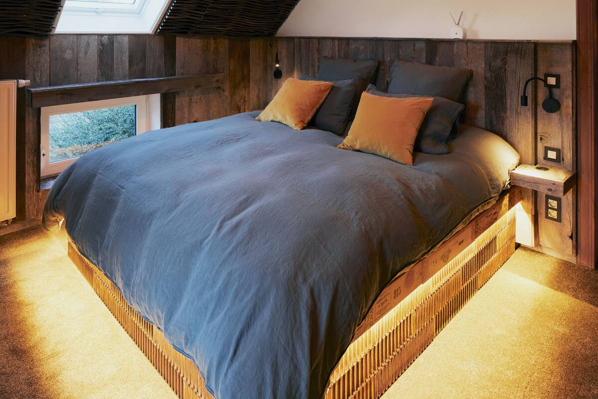 A bedroom with a sloped ceiling, a skylight, a bed with pillows, and a bedside table with a lamp.