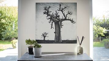 A room with a large painting of a tree on the wall, a wooden cabinet with drawers, and two potted plants on a counter.