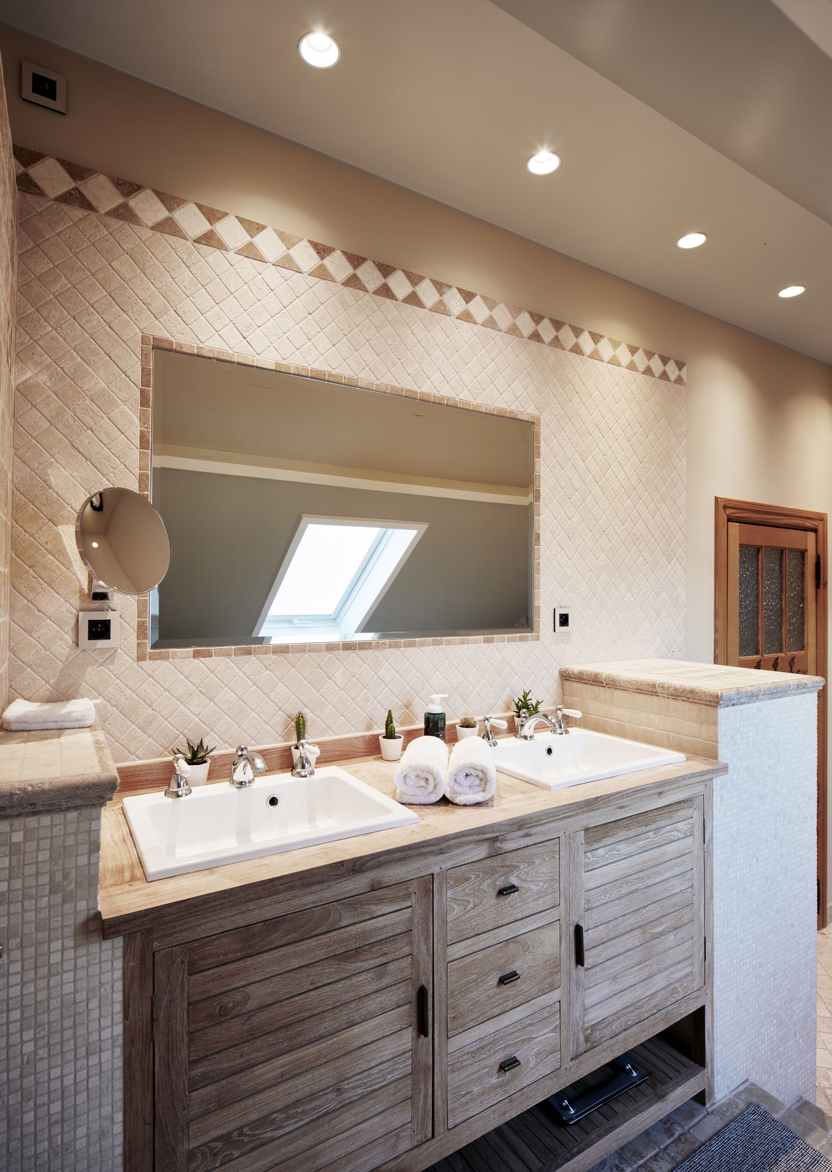 A bathroom with a large mirror, two sinks, wooden cabinets, and a tiled backsplash.