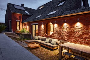 Una casa moderna con fachada de ladrillo, un banco de madera, un sofá y una mesa.