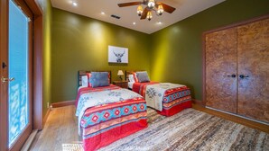 A bedroom with two beds, a ceiling fan, a large wardrobe, and a window with blinds. - Falling Star Lodge - A Sayles Ranch Home (Abilene)