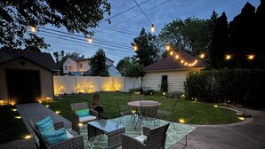 Patio sul retro con mobili da esterno, un tavolo e luci a catena.