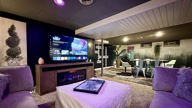 Un soggiorno moderno con una TV a schermo piatto, una console di gioco, un tavolino da caffè e un'area salotto con due divani.