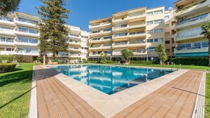 Ein modernes Mehrfamilienhaus mit einem zentral gelegenen Schwimmbad, umgeben von gepflegten Rasenflächen und Bäumen.