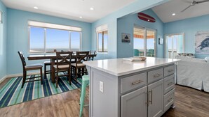Una habitación amplia con un gran ventanal, un comedor y una cocina con una isla blanca.