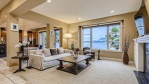 A spacious living room with a large window offering a view of the sea, a fireplace, and a cozy seating area. - Stunning Luxury Waterfront Home (Sammamish)