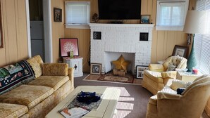 Un salon avec un ventilateur de plafond blanc, une cheminée, un téléviseur et un canapé.