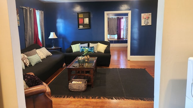 A living room with a dark blue wall, a black sofa, a wooden coffee table, and a brown leather chair. - SPACIOUS AND QUIET (Meriden)
