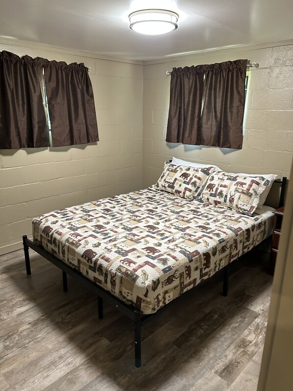 A bedroom with a bed, wooden floor, white walls, and brown curtains.