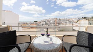 A balcony with wicker chairs and a round table, overlooking a cityscape with buildings and a clear sky. - Colibri Apartment by HelloVacations (Albufeira)