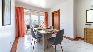 A dining area with a table set for four, chairs, a buffet counter, and a view of the city through large windows. - Colibri Apartment by HelloVacations (Albufeira)