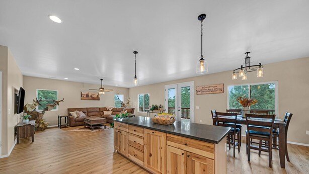 A spacious living area with a wooden floor, a large island with cabinets, a dining table with chairs, and a ceiling fan. - Serenity in the Mountain Pines at The Cypress Point Lodge (Flagstaff)