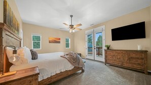 A bedroom with a bed, a ceiling fan, a dresser, a TV, and a balcony door. - Serenity in the Mountain Pines at The Cypress Point Lodge (Flagstaff)