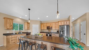 A spacious kitchen with wooden cabinets, a large island with bar stools, stainless steel appliances, and pendant lighting. - Serenity in the Mountain Pines at The Cypress Point Lodge (Flagstaff)