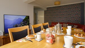 A dining area with a wooden table set for breakfast, including plates, cups, and a coffee pot. - Blue Sparrow House (Portsmouth)
