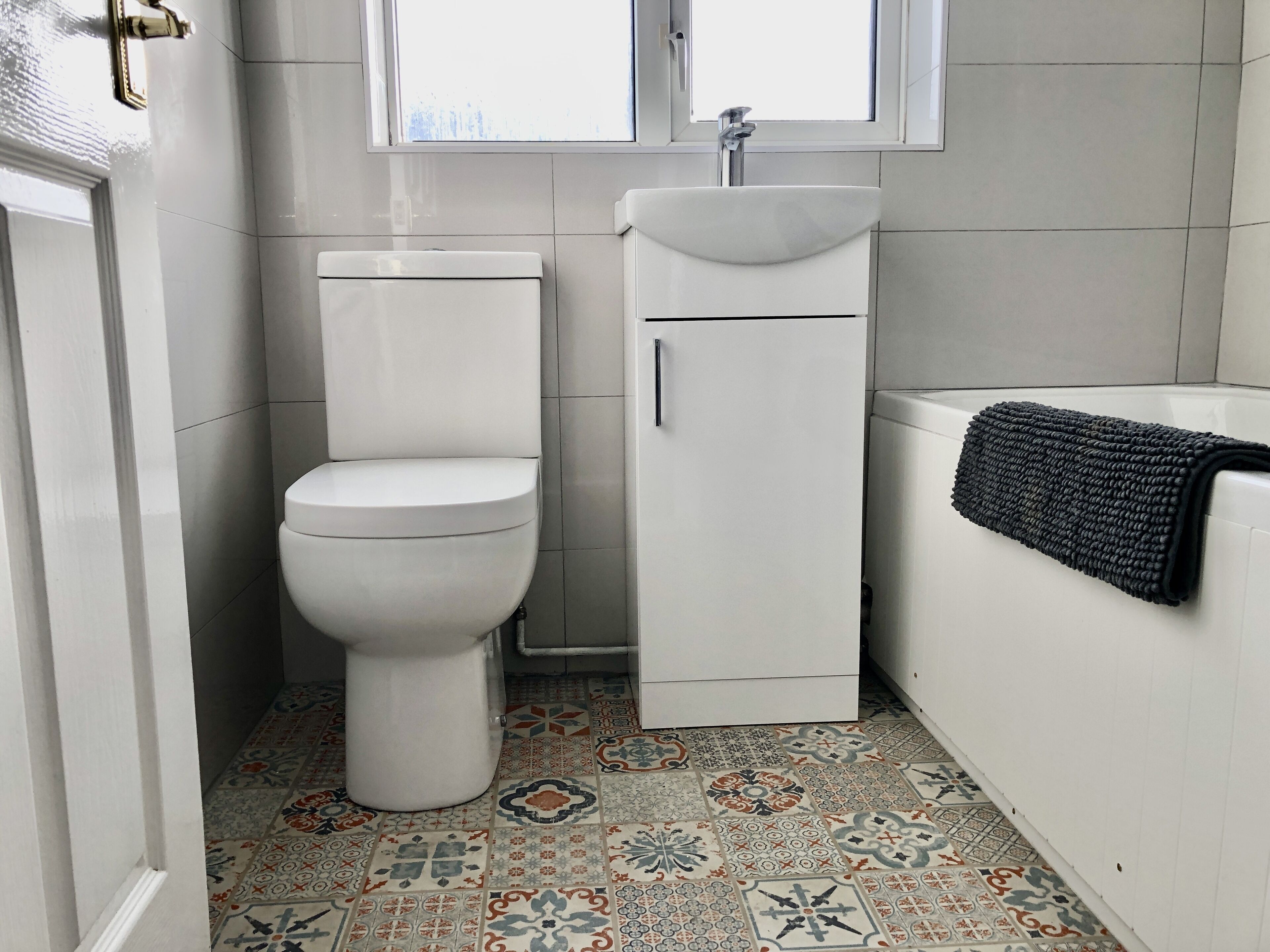 A bathroom with a toilet, sink, and bathtub. The floor has patterned tiles.